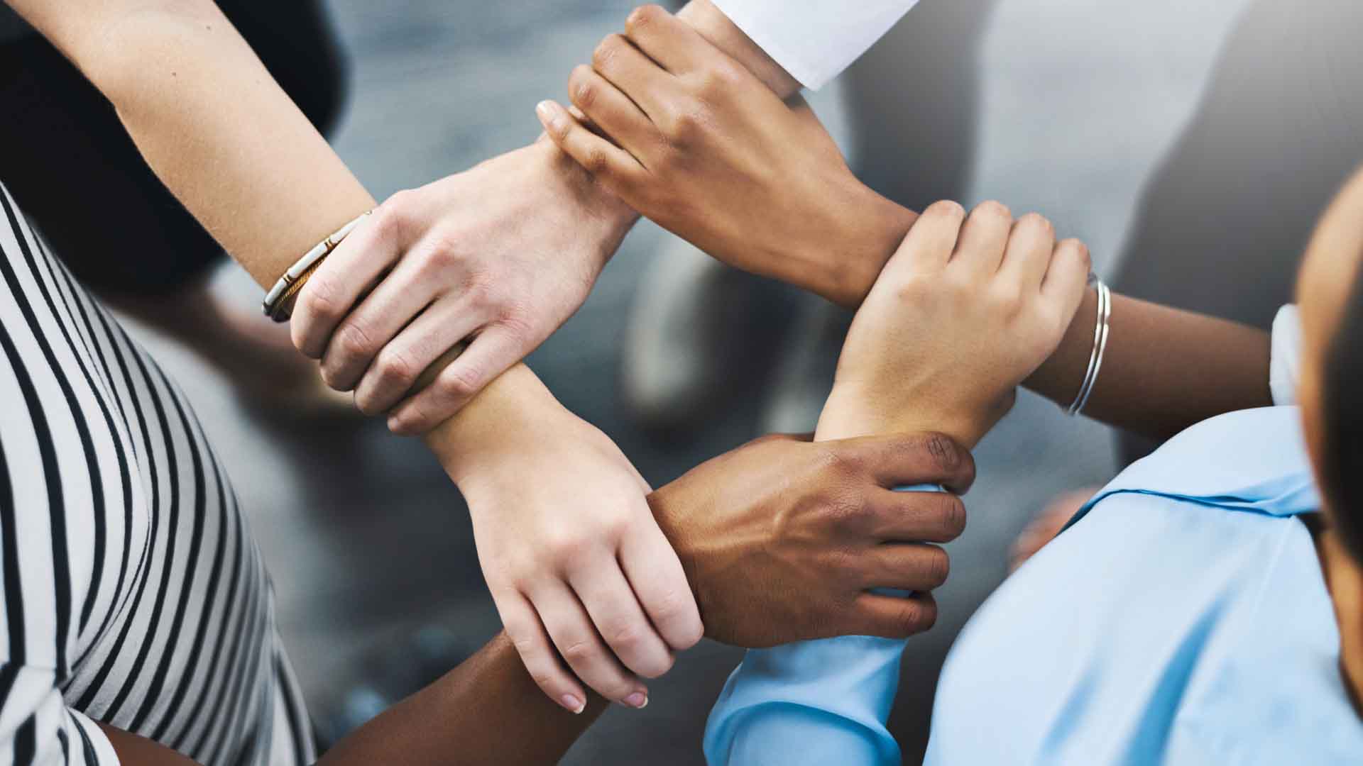 High angle shot of a group of businesspeople holding one another's wrists in a circular formation.